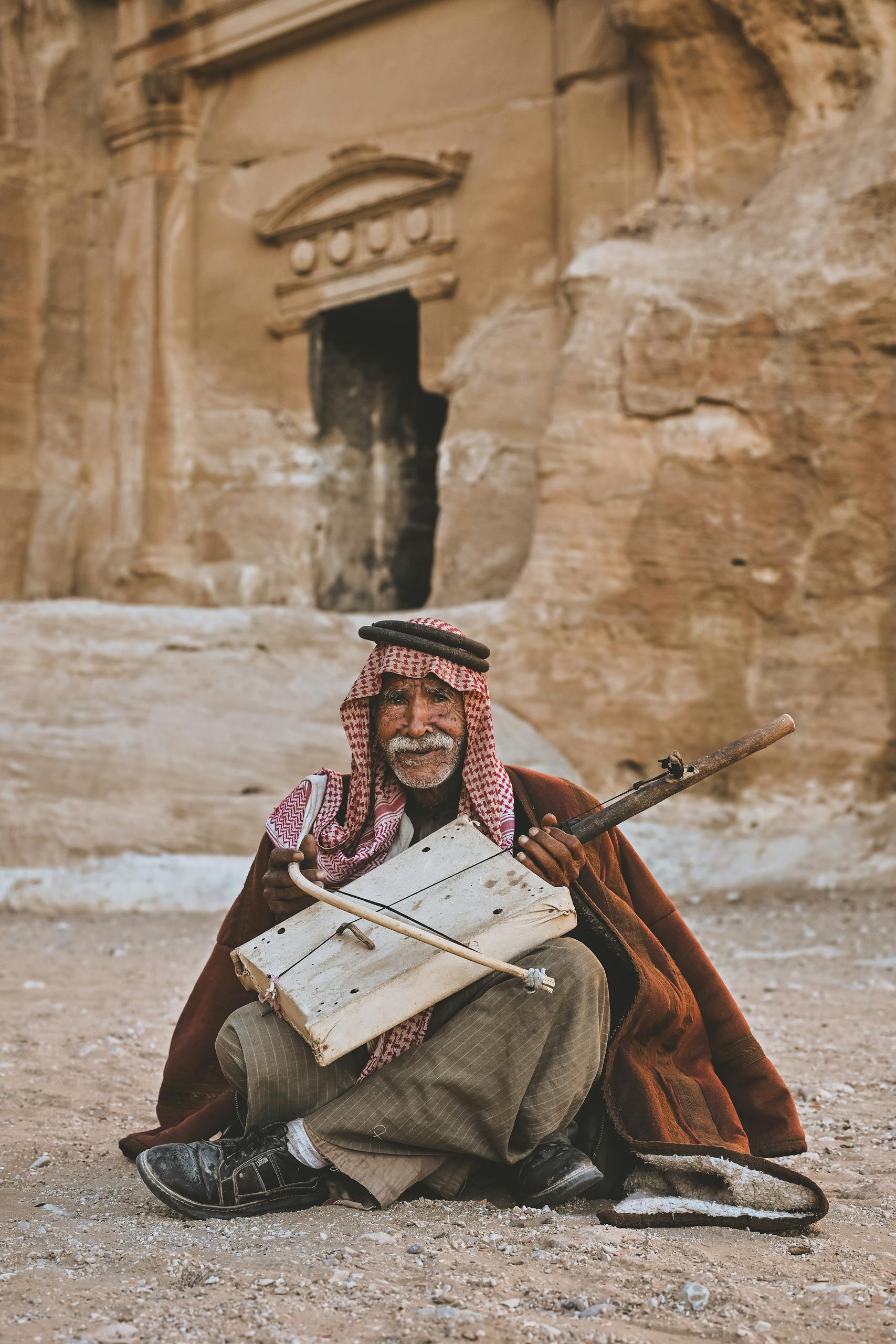 Elderly man in Petra, Jordan playing a traditional rababah against ancient rock backdrop.